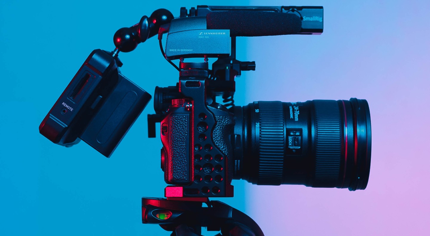 A video camera pointing right against a blue and pink background