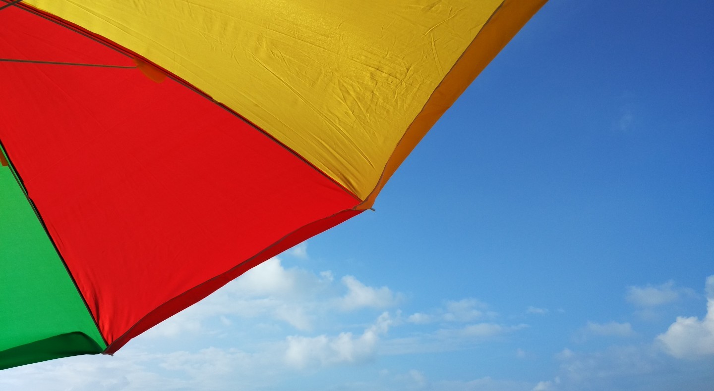A colourful rainbow umbrella is open in front of a blue sky with white clouds