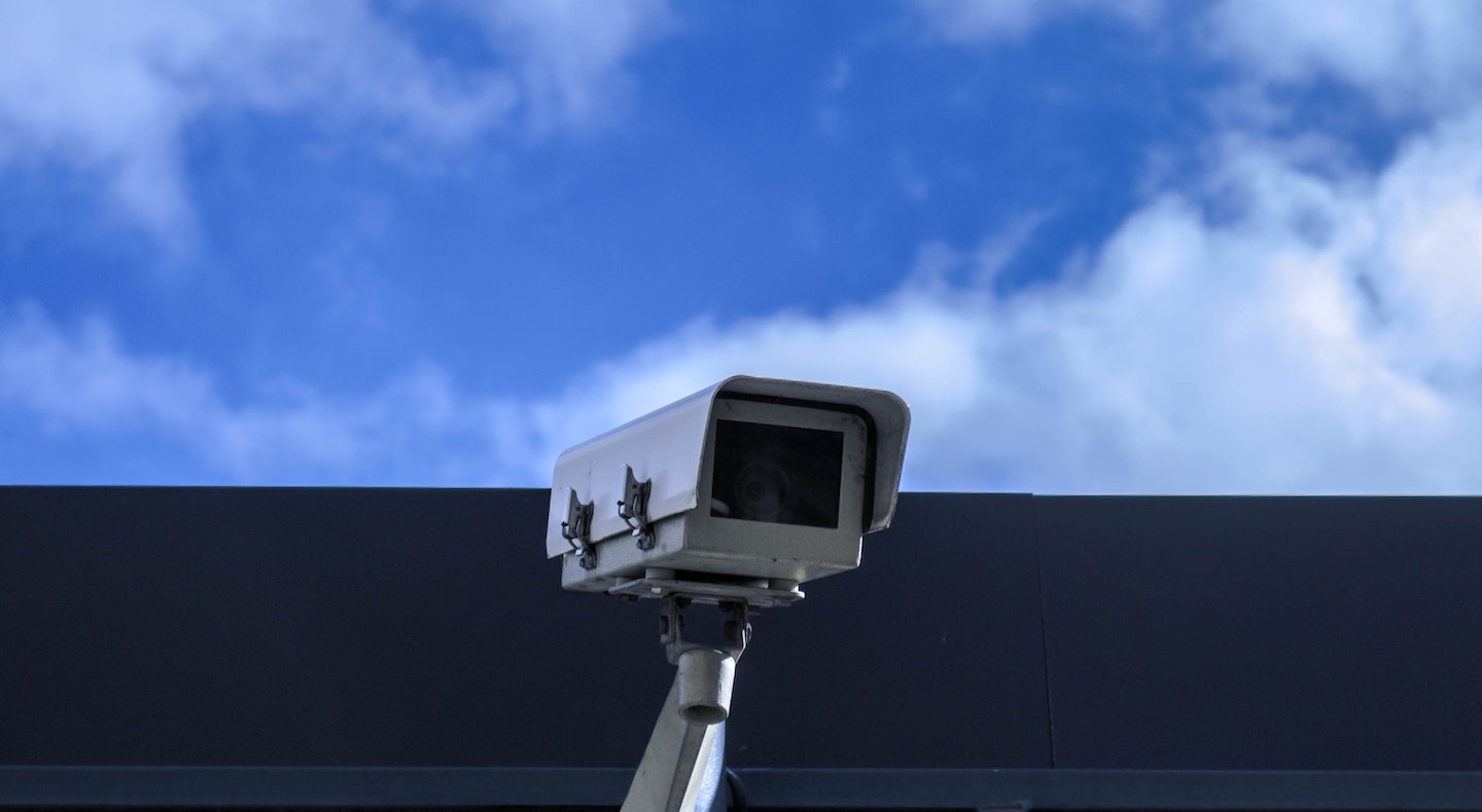 A photo of a security camera in front of a background of clouds